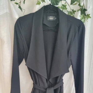 Svart trenchcoat  - Strl. M. Perfekt för sena sommarkvällar att bara hänga på sig eller för en fin touch till outfiten. Bälte medföljs. 