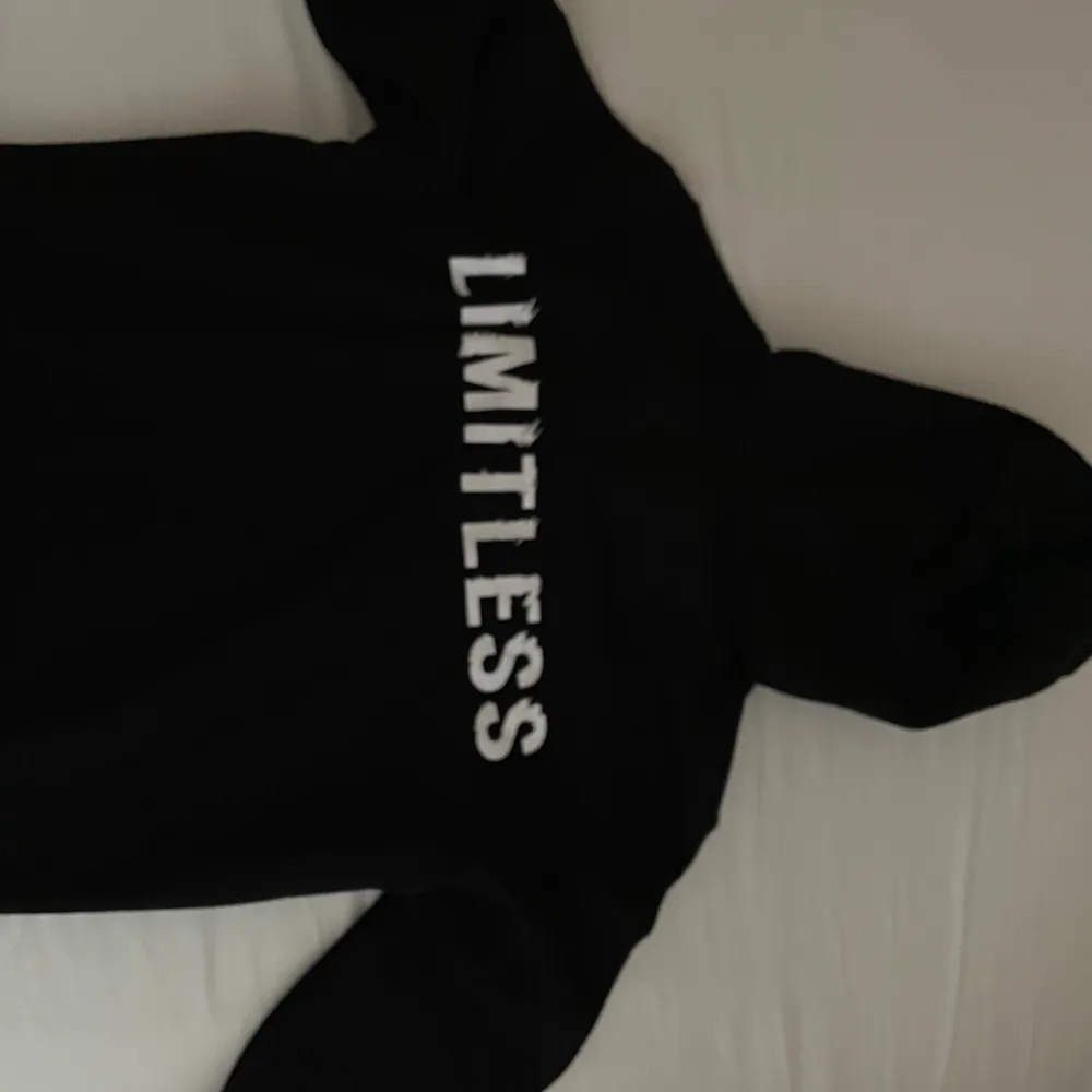 En svart hoodie med texten 'LIMITLESS' tryckt i vitt på framsidan. Hoodien har en luva med dragsko och långa ärmar. säljer på grund av storlek men passa för både L och M . Tröjor & Koftor.