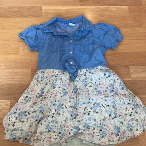 Somrig klänning - Blommig klänning med blå överdel. Använd ganska många gånger men inga tecken på slitage. Är i storlek 110 från Lindex. Bild 1: framsidan  Bild 2: baksidan 