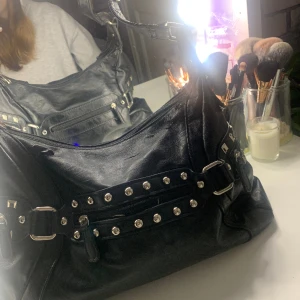 Väska med nitar - 💖Säljer en väska med nitar.💖4 fack utanpå och 3 mindre fack inuti. 30x12cm på botten. Väskan har några defekter (se sista bilden) men det kanske går o fixa. Kan skicka fler bilder och tryck gärna på köp nu💗✨🛍️❤️❤️