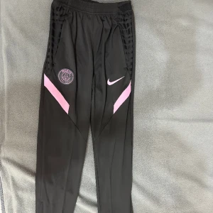 Nike PSG byxor - Svar/rosa PSG byxor, skön kvalitet. Strech material. Skicket på de är 10/10. Knappast använda. Säljer pågrund av för lite storlek.