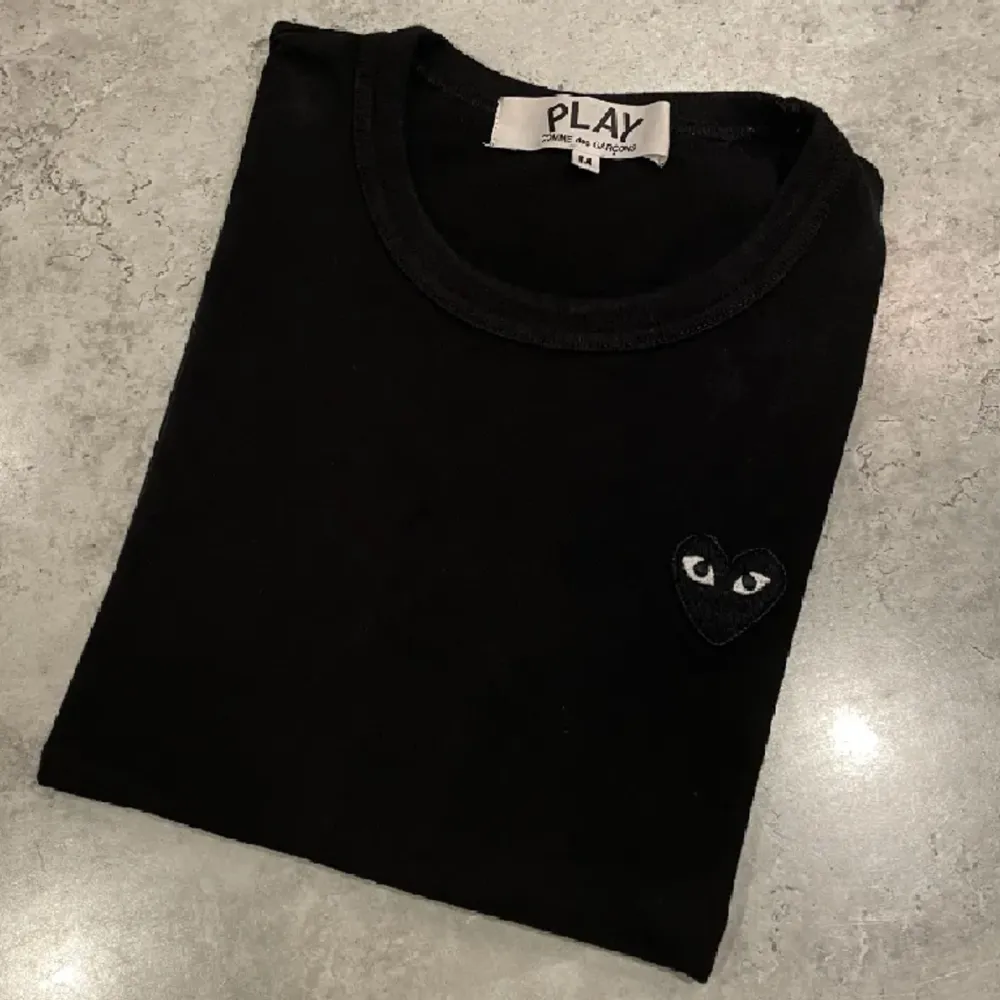 Det är en t-shirt från Comme des Garçons PLAY i färgen svart. Storleken är i M men det stämmer inte överens med den verkliga passformen. Jag skulle säga att den är i storleken XS/S. . T-shirts.