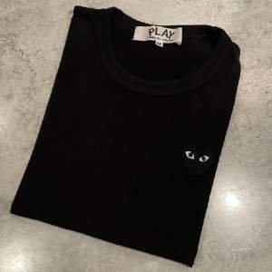 Det är en t-shirt från Comme des Garçons PLAY i färgen svart. Storleken är i M men det stämmer inte överens med den verkliga passformen. Jag skulle säga att den är i storleken XS/S. 