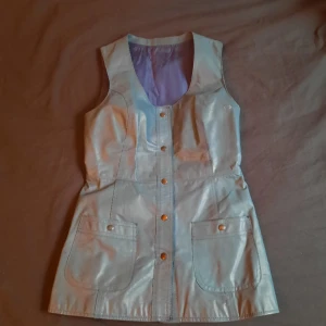 Retro läderklänning! - Blå/turkos retro läderklännig med tryckknappar där fram! Kan även användas som en lång väst;> Köpt secondhand på 90-talet men därefter knappt använd. Önskar jag kunde ha den men säljer då den är för stor:(