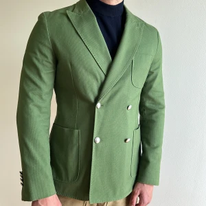 Kavaj dubbelknäppt J. Lindeberg sz 48 - Grön kavaj från J. Lindeberg. Dubbelknäppt med elegant och unik modell! Storlek 48. Felfritt skick. 100% bomull.