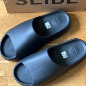 Adidas Yeezy Slide - Storlek EU: 47 Mindre i storleken. Passar 46 & 46 2/3  Skick 10/10 oanvända  Färg: svart  Kvitto och kartong förljer med skorna vid köp.  Skorna skickas spårbart med Postnord 