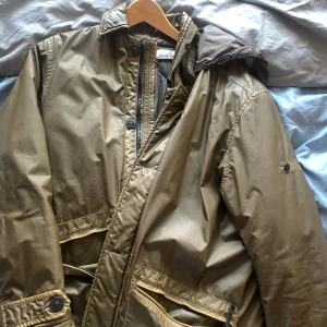 Stine island mussola gommata  - Vaxad textiljacka, inte vattentät men går bra om det bara e lite regn. Fickan på ena sidan e sönder men kan lätt fixas hos skräddare. Även ihopfällbar luva 