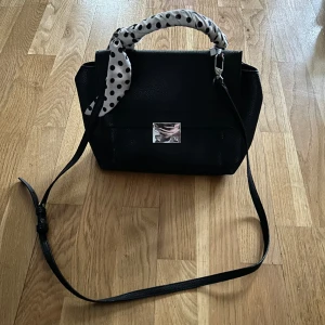 Väska  - Svart väska med avtagbara långa axelband som också går att justera, i använt men mycket bra skick! Lite skrapad på spännet bara. 