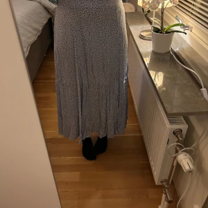 Medellång kjol - Säljer en blå kjol med vita blommor från H&M. Storlek 40. Sitter lågmidjad på mig eftersom jag brukar ha storlek 36. Ska sitta som hög/medel midjad. Har slits på sidan. Jag är 161 cm för referens. 