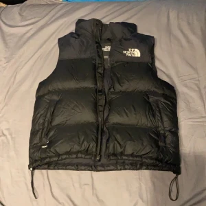 The North Face Väst - Skick: 9/10 Storlek: L En svart lite tjockare dunväst av märket The North Face. Säljs pågrund av att jag inte använder den längre. Västen är i top skick pågrund av sparsam användning. Möts i Stockholm City.