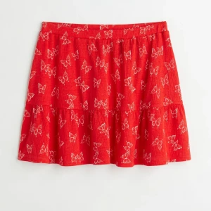 Sommar kjol,M - En kort kjol i mjuk trikå med tryckt mönster. Kjolen har normalhög midja med dold resår. Avskärning nedtill med bred volangkant. Ofodrad. Normalhög midja Passform: Regular fit Röd/Vit, Mönstrad, Fjärilar I mycket fint skick, sparsamt använd