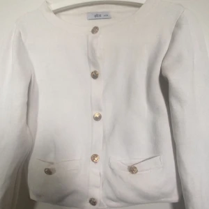 Vit kofta - Säljer nu en jättefin kofta med guldiga knappar. Koftan är använd men är i fint skick! Den är i strl 24/30 men passar som xs/s. Passar till många olika outfits.