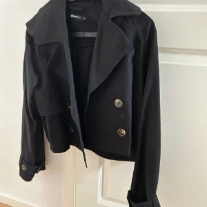 Svart kort trenchcoat  - Helt ny svart trench coat, går att styla med nästan allt. Brukar vanligtvis ha xs-S men tog xxs på denna då den är riktigt stor i storleken 