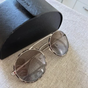 Prada solglasögon - Köpta i Frankrike använda sparsamt men lite skav i glaset. Inget som man ser eller tänker på när man bär dom. Kommer med glasögonfodral😊 Silver båge med gråmelerad kant Nypris ca 3000:-