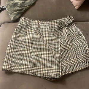 skort (kjol/shorts) med rutigt mönster  - ett par shorts som ser ut som en kjol, väldigt bekväm utan risk att råka flasha någon. Använd ett par få gånger men är tyvärr för liten nu. Den har en rutig typ av möster i färgerna svart vit och brun. (pris kan diskuteras vid snabba köp!)