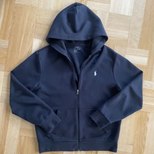 Ralph Lauren ziphoodie - En svart Ralph Lauren hoodie utan några skador eller hål🔥 Snörena är utdragna, det finns en jätteliten solblekning längst nere på hoodien men den är knappast synlig. Höra av dig vid frågor🤩