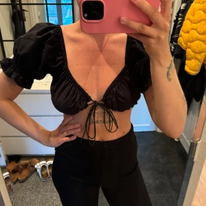 Svart crop top  - Svart crop top med knytdetalj fram, puffärmar. Från Chiquelle i stl S. Normal i storlek. Använd men i mycket fint skick!!