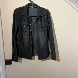 Jeansskjorta  - Säljer då jag inte använder den. I bra skick och passar perfekt att ha till sommaren på kvällen när det blir lite svalare. Mörkgrå nästintill svart i färgen