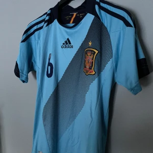 Fotbollströja - Hej, säljer nu denna riktigt feta retro Spanien fotbollströja säsong 2012-2013 med Iniesta på ryggen. Väldigt fint skick skulle jag säga 8/10. Finns inga defekter, allt är original. Priset går att diskutera vid snabb affär🤝🏼Hör av dig vid minsta lilla
