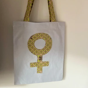 Tygkasse, tygväska, tygpåse  - Handsydd tygkasse med motivet ”feminist”.   Tillverkad i 100% återvunna textilier.   Mått: 32x35 cm  Hämtas på Södermalm alternativt skickas med post. 
