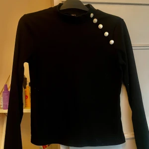 Snygg svart topp guldknappar S - Snygg stilig topp med guldknappar på axeln. Oanvänd storlek S