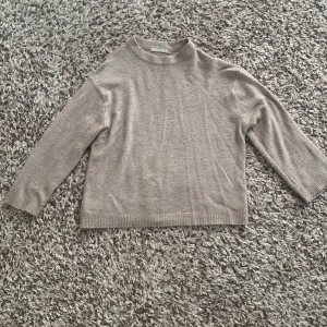 Grå stickad tröja från 139 - En enkel och stilren grå stickad tröja från märket 139. Tröjan har långa ärmar och en ribbstickad kant vid ärmslut och nederkant.