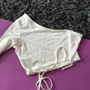 Vit topp - One shoulder tröja, kort i modellen men normal i armaren. Gott skick aldrig använt. Snören där bak (man kan knyta hur man vill)