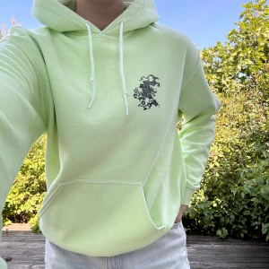 Cool hoodie med motiv - JÄTTECOOL, ljust neongrön hoodie med motiv på fram samt baksida🤩! Vita, svarta och orangea drak-motiv. Då det var en favorit har den tyvärr några mindre fläckar, se bilder + någon mer. Storlek: S (fungerar för M). Material: 50% bomull 50% polyester.