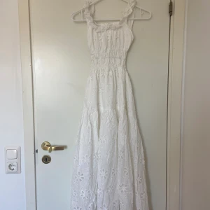 Vit klänning med blommönster  - Vit långklänning med slits och öppen rygg med blommönster i nytt skick. (Bortklippt lapp)  Frakt tillkommer, plagg som köps kan samfraktas!