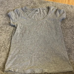 Grå t-shirt från 157 - En enkel och bekväm grå t-shirt från märket 157. T-shirten är tillverkad av 85% bomull, 10% viskos och 5% elastan, vilket ger den en mjuk och stretchig känsla. Den har korta ärmar och en rund halsringning.