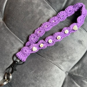 Nyckelband  - Egenvirkat nyckelband i lila bomullsgarn med pärlhjärtan och texten ”LOVE” på och en svart karbinhake som avslut. 20 cm lång och ca 30 cm i omkrets. Passar perfekt på handleden eller i din ficka.