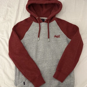 Superdry hoodie - Röd/grå hoodie från Superdry i storlek S. Köpte den för ca 1 år sen men har knappt använt den. Säljer nu eftersom den inte riktigt passar mig längre.