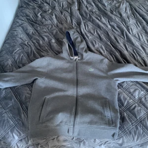 Lacoste Zip Hoodie - En väldigt skön och tjock Lacoste hoodie i vintage grå färg som har blivit så populär. Skicka ett meddelande så löser vi pris