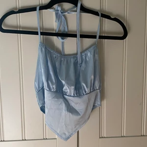 Ljusblå glansig festtopp - Ljusblå cropad festtopp i glansigt material med  resår baktill och knytning runt halsen.  Köpare står för frakt. Hör av dig vid intresse.