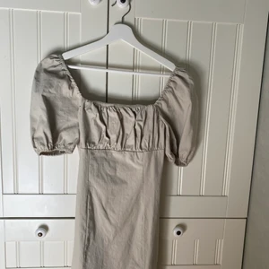 Beige tajt klänning med puffärm - Beige tajt klänning med puffärm och fyrkantig halsring och smock framtill. Endast använd vid några få tillfällen så fint skick.  Köpare står för frakt. Hör av dig vid intresse.