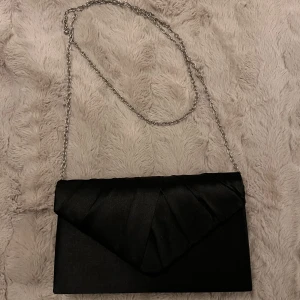 Kuvertväska - Liten väska. Hårt material, telefonen ryms i den. Använd en gång. Silvrig kedja. Hade den på min studentbal och passade super fint.