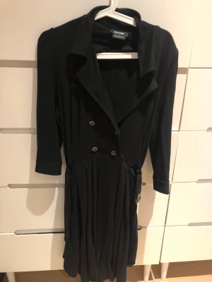 Svart klänning med trenchcoat vibes💕 - Den är köpt secondhand men har aldrig blivit använd:( Den har lite trenchcoatiga vibes och klänningens kjol är indelad i shorts. Men ser ut som en klänning på💕Har bälte<3