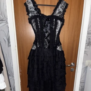 Korsettklänning svart/silver - Säljer denna korsettklänning från c.u.m clubwear. Kjolen har fem lager och är ganska kort i fram men lång i bak. Endast använd en gång. Originalpris: 1400 kr.