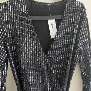 Glittrig klänning  - Glittrig klänning från Gina. Glittrig skärp som sitter med klänningen.  Oanvänd och lapparna sitter kvar. Storlek L  