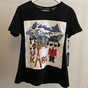 T-shirt med tryck, Karl Lagerfeld - T-shirt med tryck från Karl Lagerfeld, med 3D material på öronmuffarna. Helt ny, oanvänd med lappar kvar. Perfekt till afterski men funkar också till vardags. 