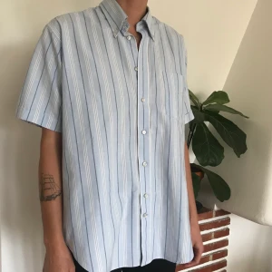 Ljusblå kortärmad skjorta  - Kortärmad skjorta ljusblå randig från VanHeusen. Står storlek 42 i men jag skulle säga L/XL! Snygg boxig form med rundad nederkant. Kan mötas upp i Malmö eller Lund eller skicka!