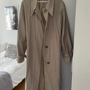 Trenchcoat från Asos - Säljer nu denna höst/vår trenchcoat från asos egna märke. Storlek 36. Köpt för 900kr, säljer för 250kr. Fint skick!
