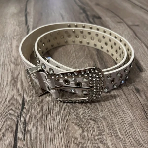 Bb Simon vit bält med stenar - Säljer detta bälte som är en dupe på bb simon. Helt oanvänt endast testad. Säljer då det inte är min stil. Bältet är 110 cm långt men går att justera 🫶🏼 Sista bilden är lånad