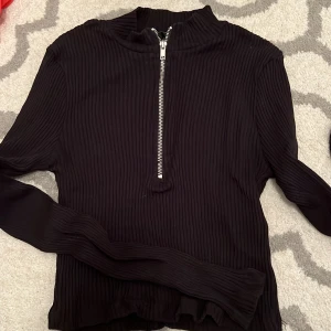 Svart ribbad topp med detalj - En fin svart ribbad topp med silver dragkedja från Gina tricot i storlek M. Använd max 2 gånger. 