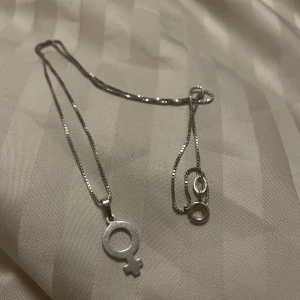 Feminist halsband - Jättefint halsband med snygg symbol i äkta silver. Både kedjan och smycket är i äkta silver. Den är aningen repig som man ser på bilden men verkligen inget som syns när man har på sig den. 