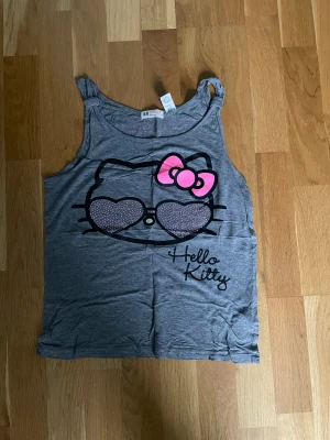 Hello Kitty linne - Sött Hellokittylinne med rhinestones på framsidan. Det står ingen storlek men uppskattar på XS-M beroende på hur tajt man vill ha den! 