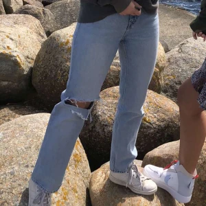 Straight blå jeans med hål i knät  - Straight jeans från Weekday i modellen VOYAGE. Superfin ljusblå urtvättad färg med ett egetklippt hål i knät som en fin detalj. Fint skick. Storlek 36. Skriv för fler bilder!