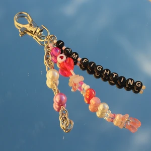 Smycke - Keychain som man kan ha som dekor både på nycklar,väska, plånbok och mer.  Smycket är handgjort för att stödja psykisk hälsa och har rosenkvarts inkluderat på sig. 20% av priset går till organisationen som showar med psykisk ohälsa. 