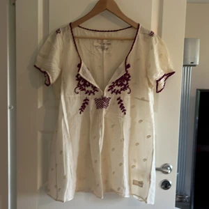Skir kort ärm blus från Odd Molly - Skir blus strl 3 från Odd Molly Beige/vit med små brodyr på hela samt mer synlig brodyr fram i vinröd/lila Köpare står för frakt