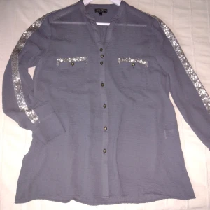 Grå blus/skjorta med glitter/paljetter, storlek 36/38 - Blus i en skitsnygg grå färg med silverfärgat glitter. Lite oversize i modellen. Snygga knappar, glittriga revärer och sprund i sidorna. Storlek 36/38 men skulle säga att den kan passa XS-L, beroende på hur man vill att den ska sitta. Sparsamt använd.